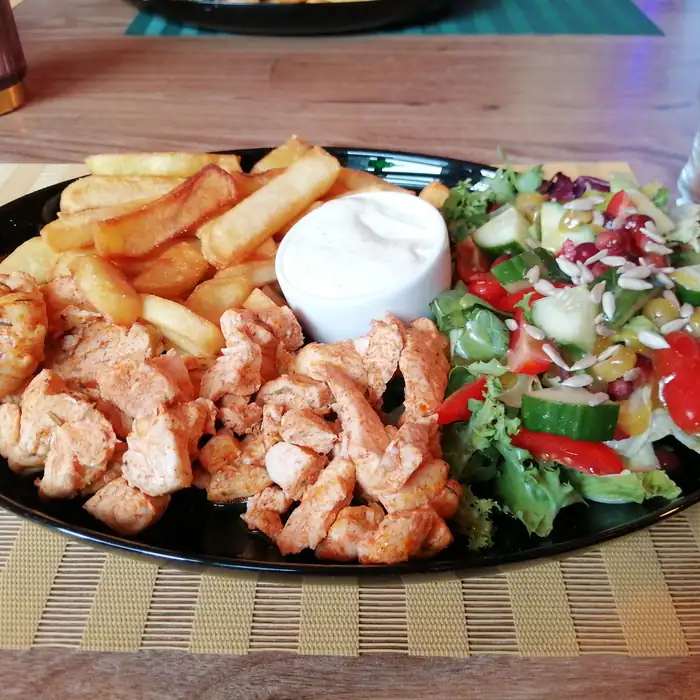Talerz z kawałkami kurczaka, frytkami, surówką i sosem czosnkowym