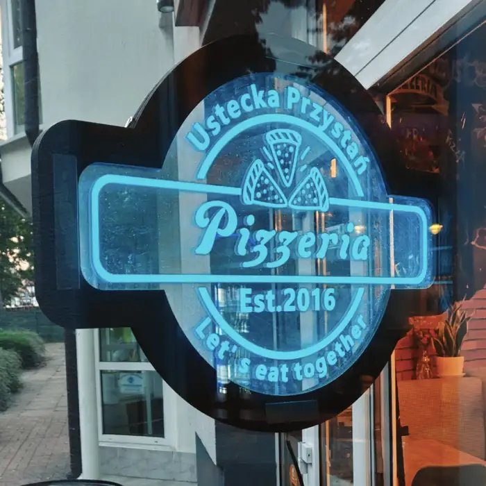 Okrągły niebieski neon Ustecka Przystań Pizzeria Est. 2016 w oknie