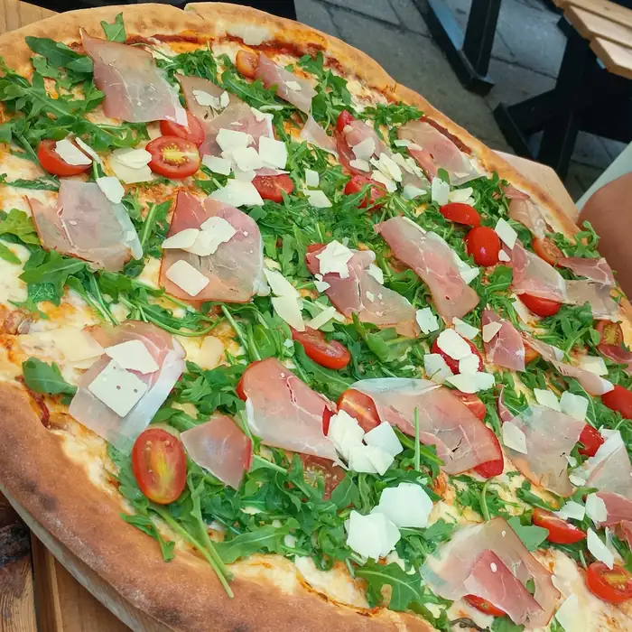 Duża pizza z szynką, rukolą i parmezanem na stole